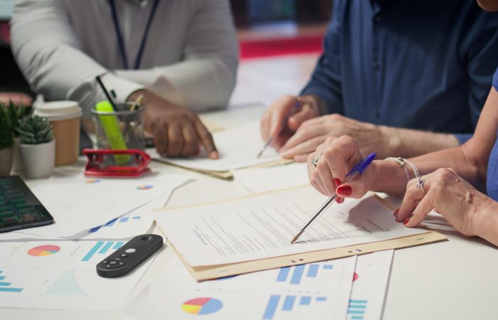 Mature person signing a contract with insurance agency banker, agreeing to the new pension plan contract with expert. Retired man collaborating with advisor to secure his life savings. Camera B.